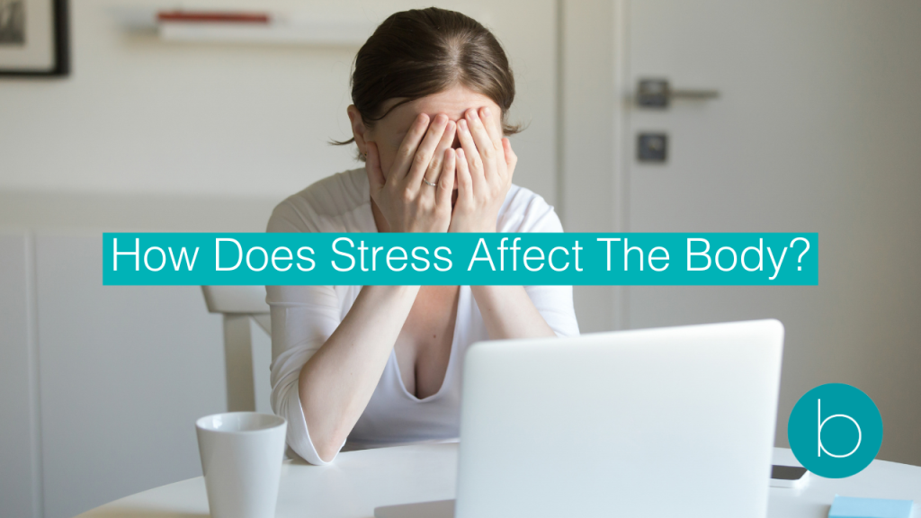 Stressed woman sitting at a table with her head in her hands in front of a laptop, highlighting the emotional and physical toll of stress.